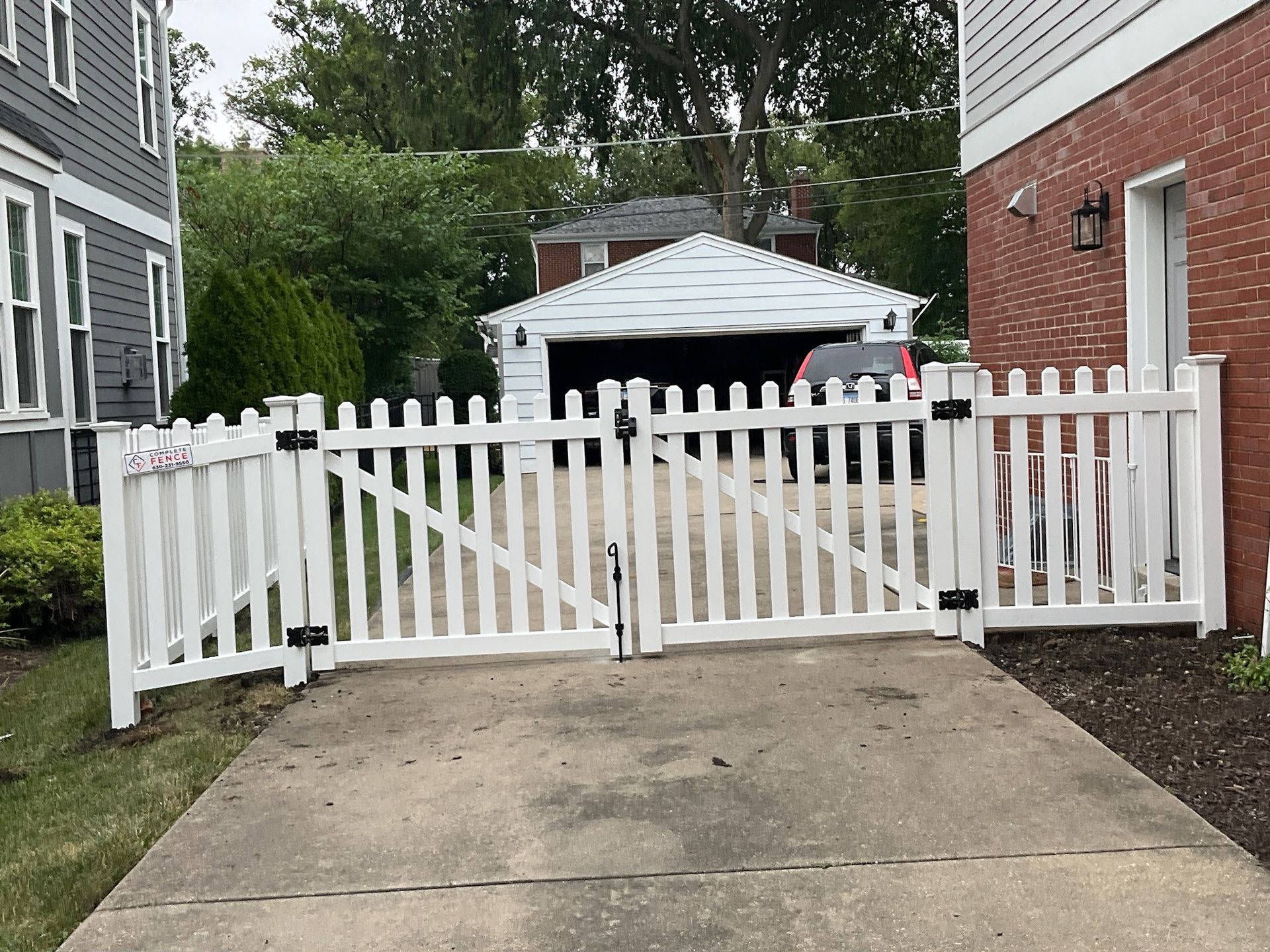 White picket fence with gate across a concrete driveway, leading to a garage.