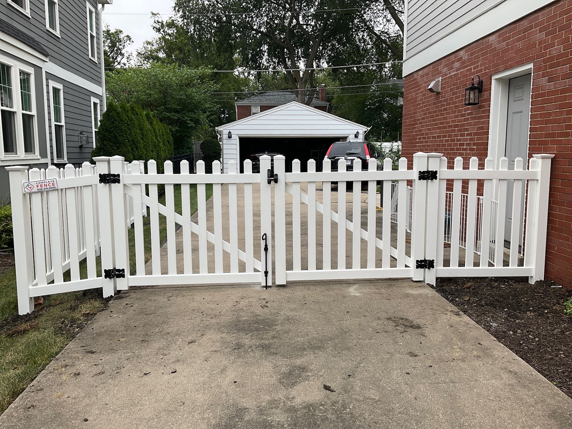 White picket fence with gate across a concrete driveway, leading to a garage.