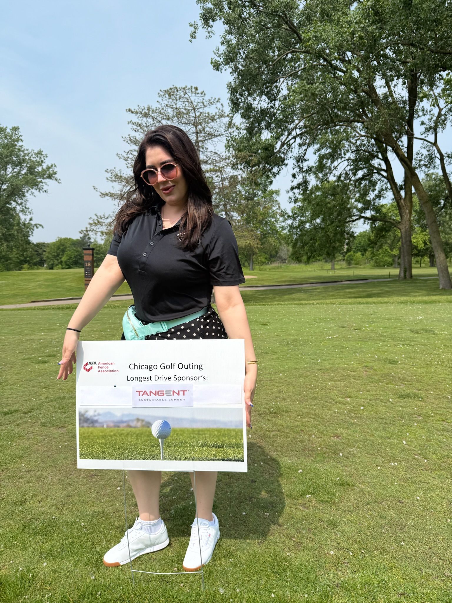 Woman on golf course holding a sign with a golf ball image; sunny day.