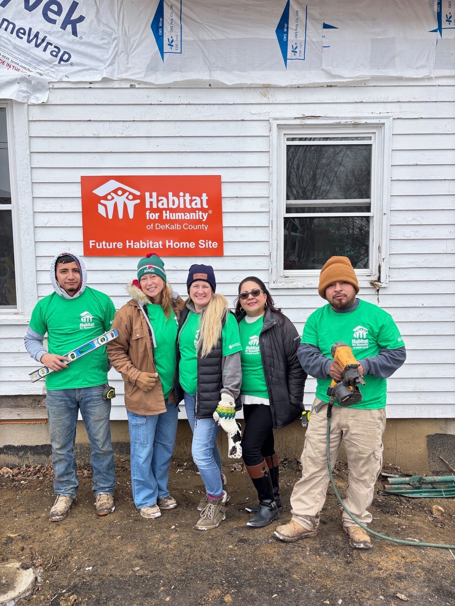 Group of Habitat for Humanity volunteers in green shirts pose in front of a house under construction.