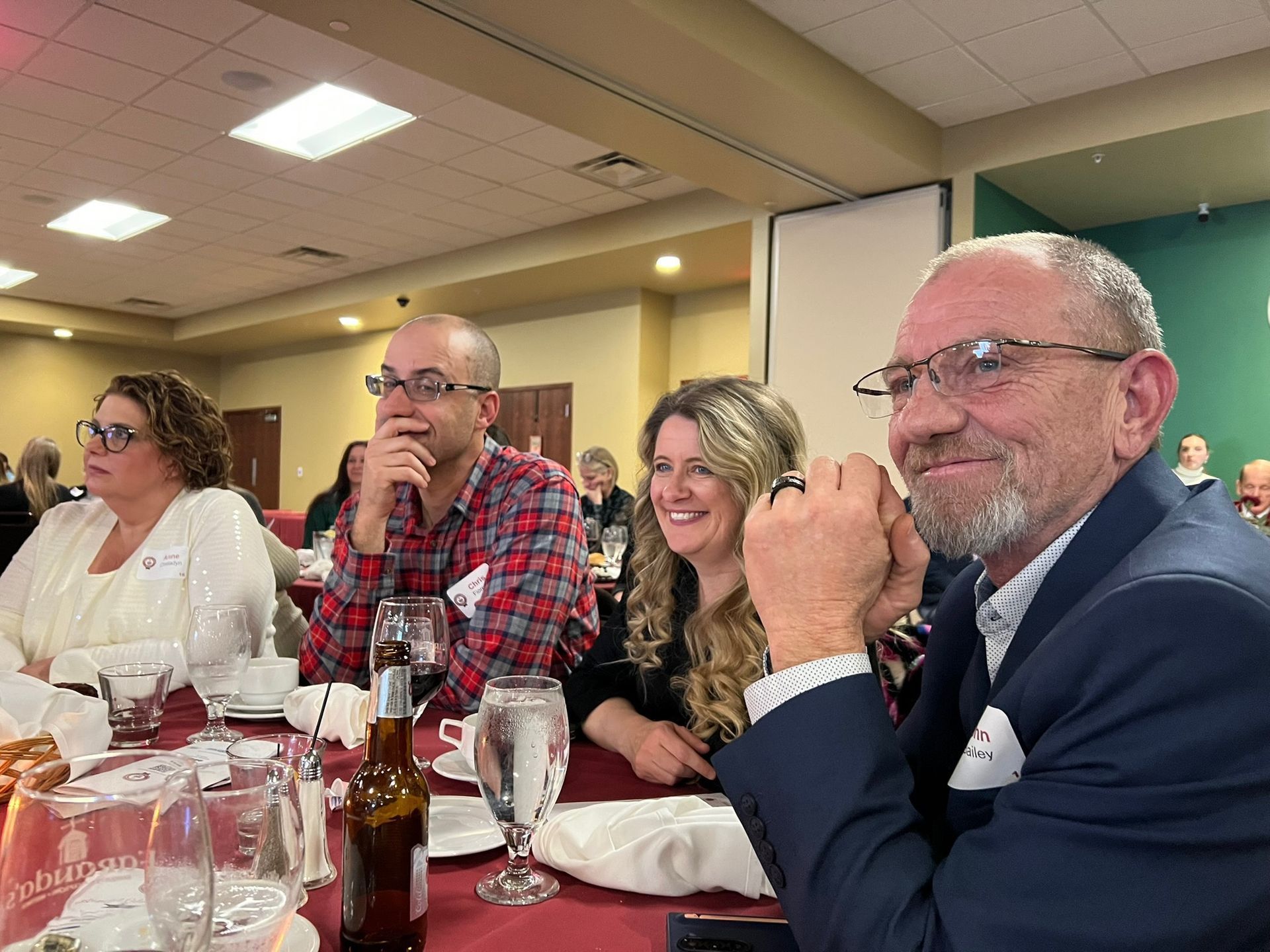 People seated at a table in a banquet hall, smiling, and looking ahead.