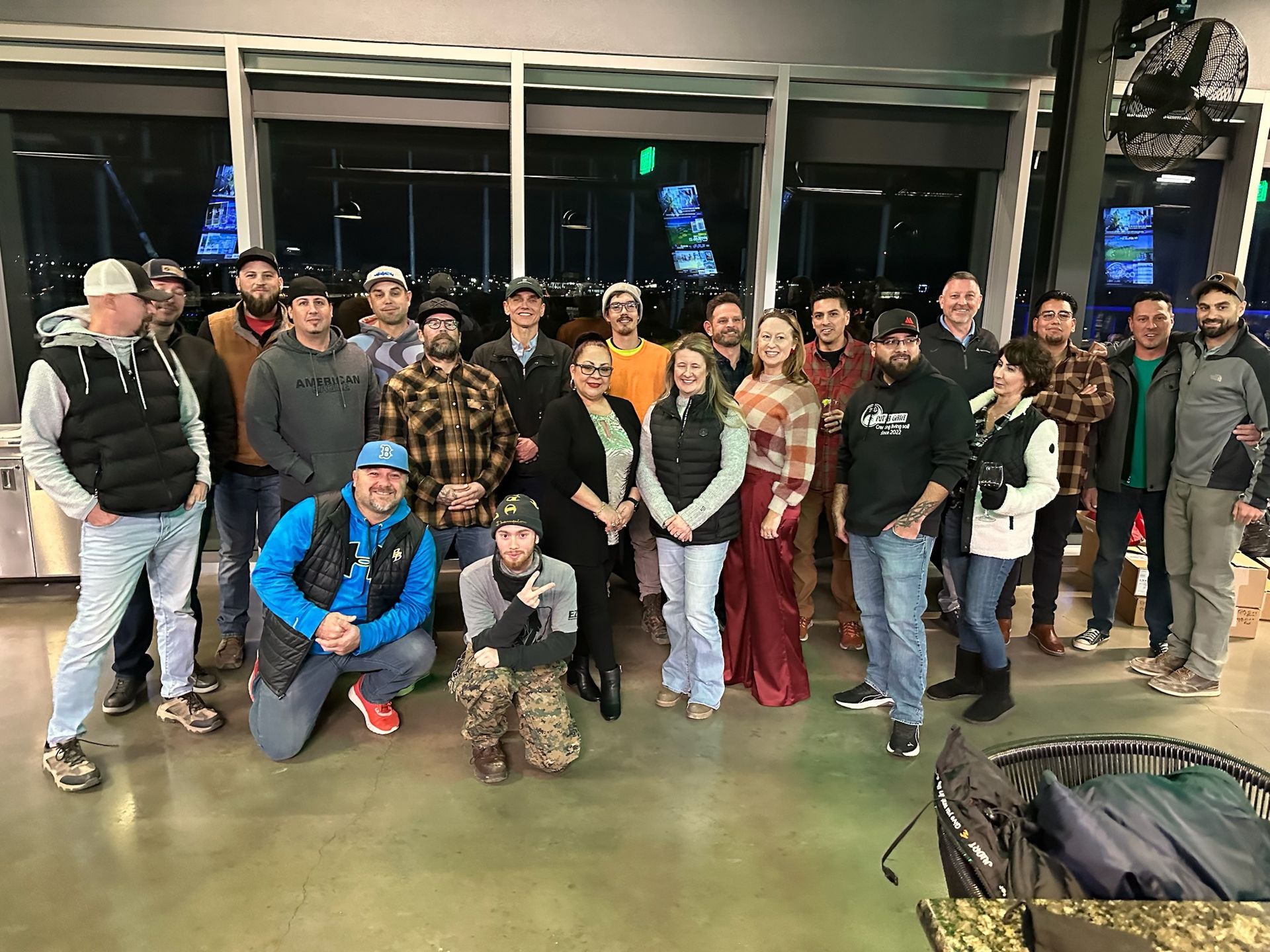Group of people posing together inside a Topgolf-like venue, smiling, some wearing casual attire.