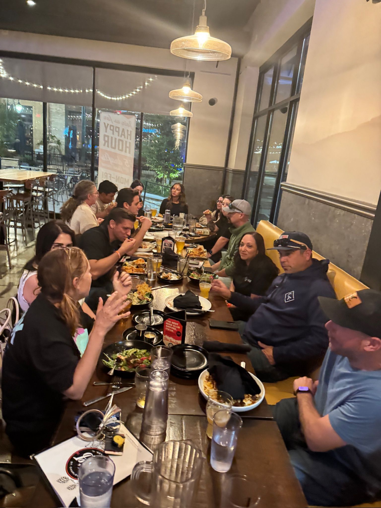 A group of people seated around a long table at a restaurant, dining and conversing.