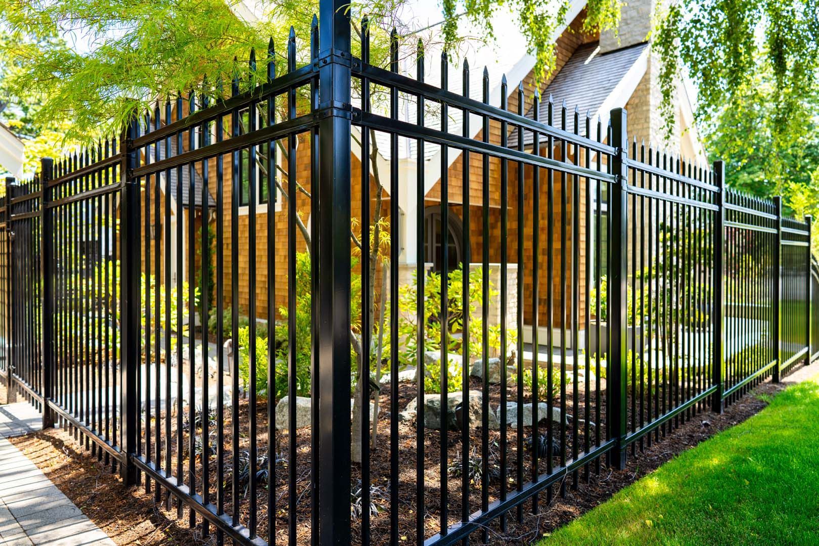 Black metal fence surrounding a yard with a house visible in the background.