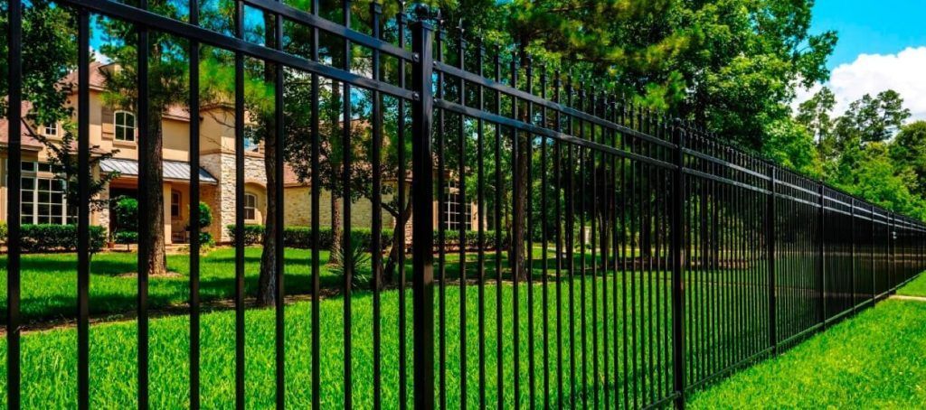 Black metal fence in front of a house, surrounded by green grass and trees.