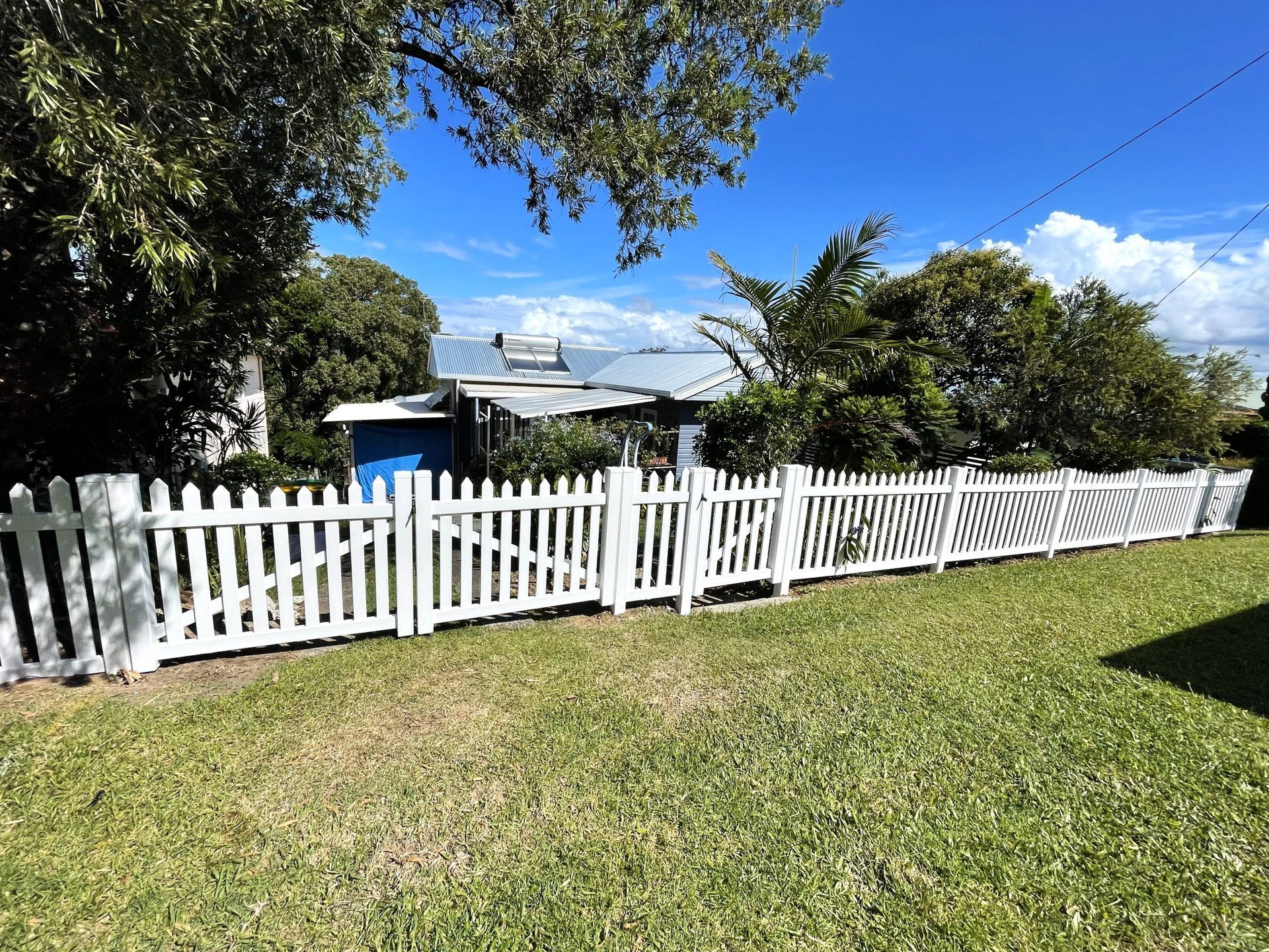 White picket fence in front of a house, sunny day, green grass.
