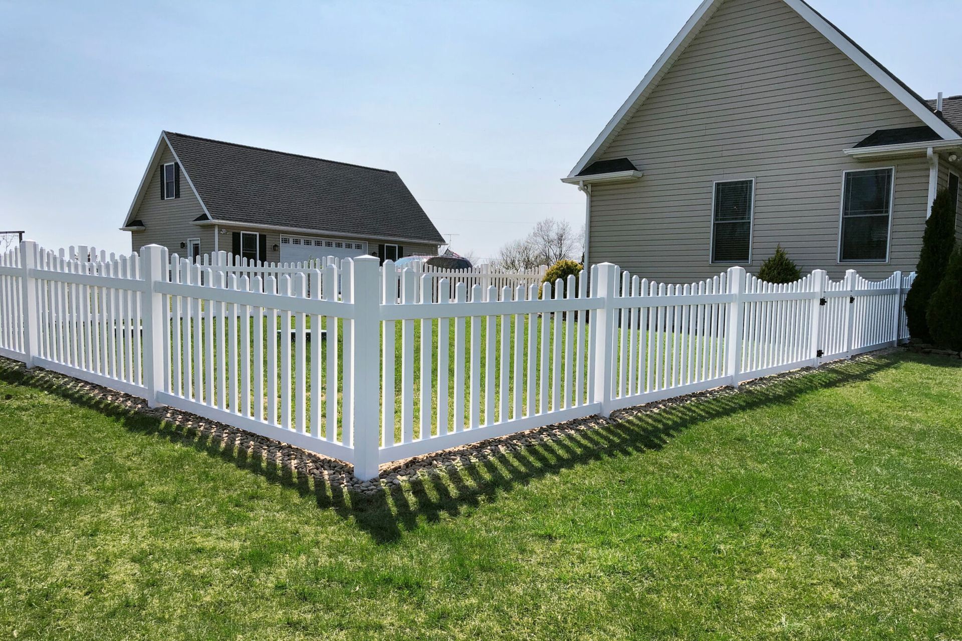 White picket fence around a grassy yard, with two houses in the background.