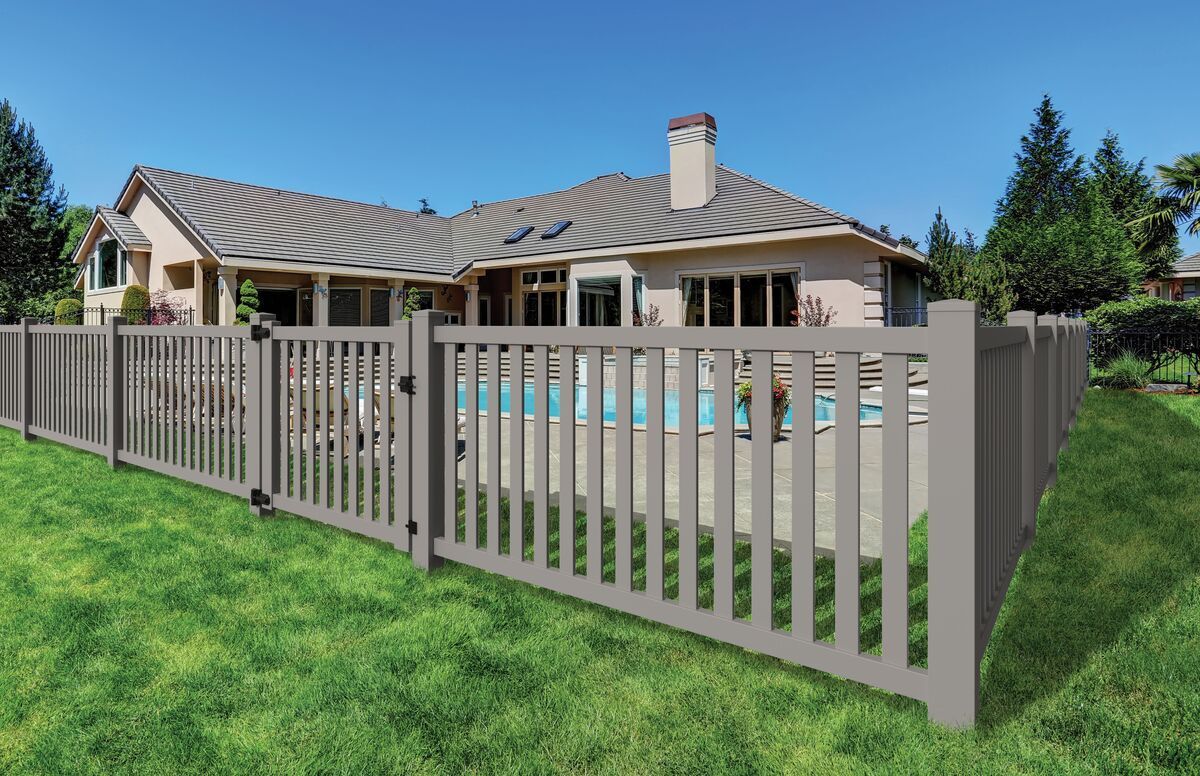 Gray picket fence surrounding a pool and a beige house on a sunny day.