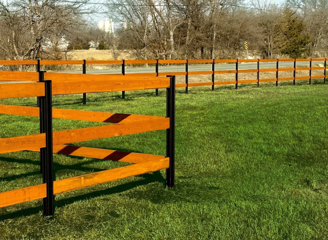 Wooden fence with brown planks and black posts in a grassy field.