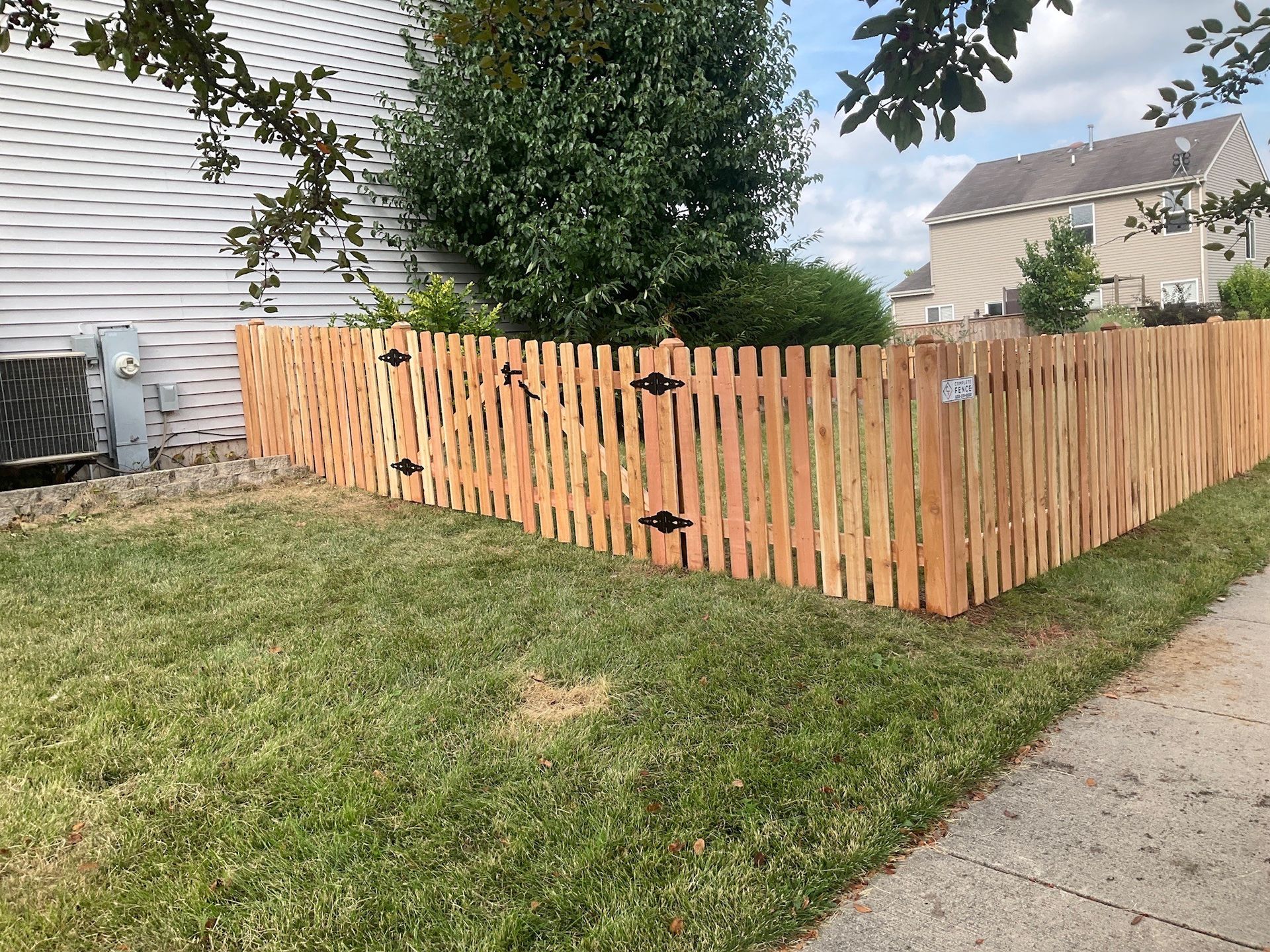 Wooden picket fence surrounding a yard with green grass and an air conditioning unit.