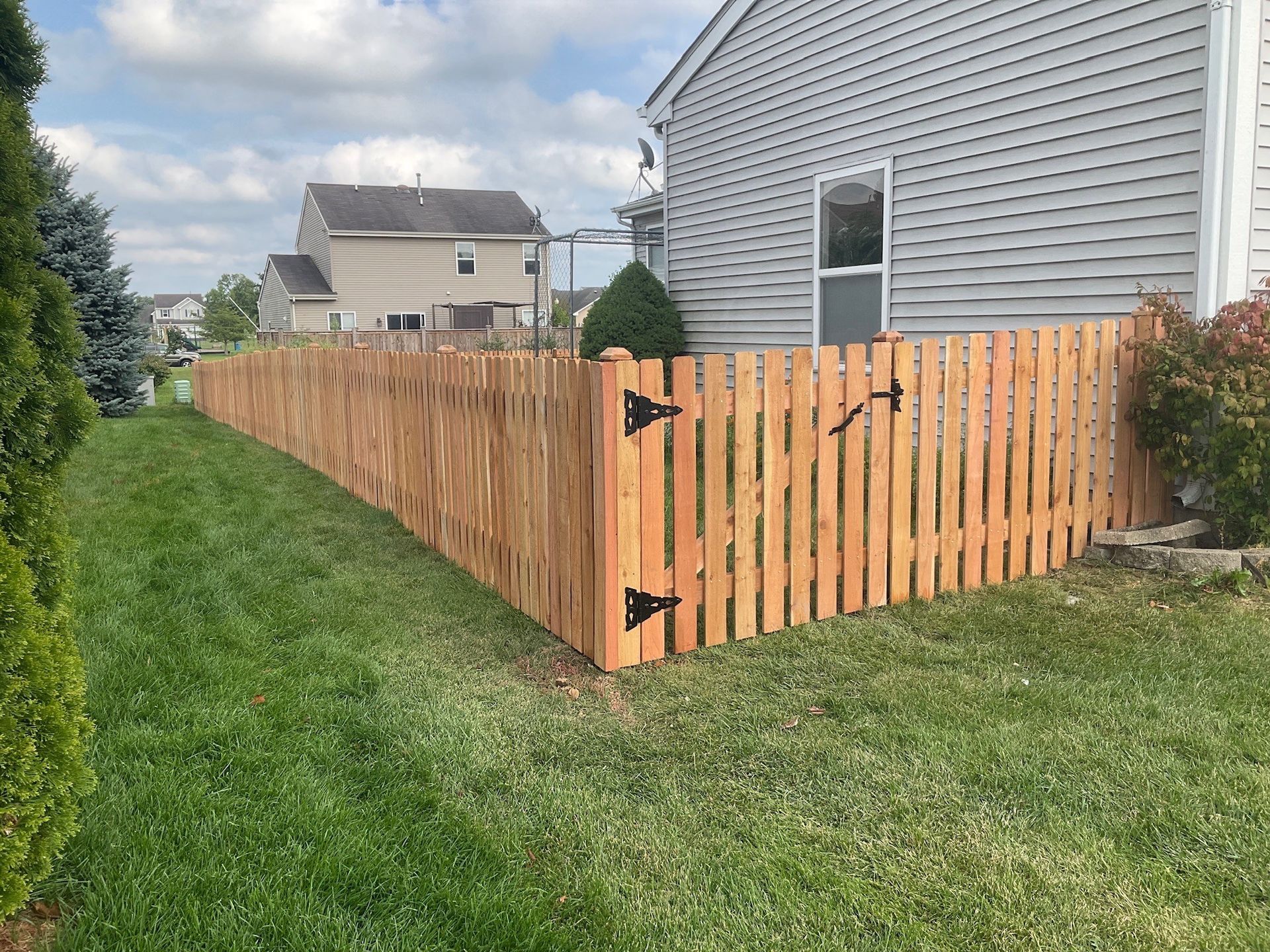 Wooden fence with gate in a grassy backyard. Beige house in the background. Sunny day.