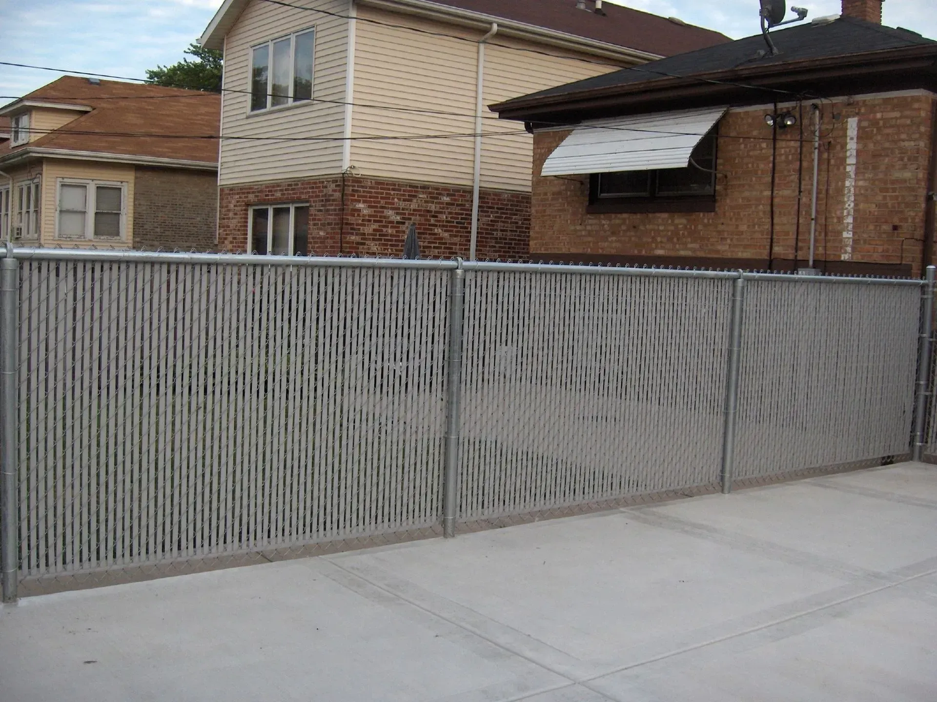 Metal fence with textured design in front of brick buildings and concrete.