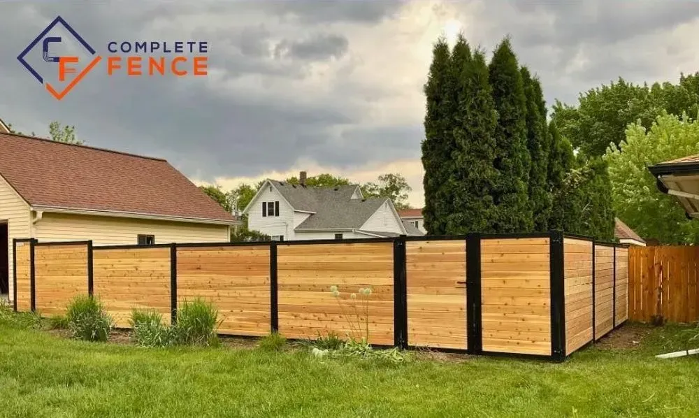 Wooden fence with black frame, protecting a backyard, under a cloudy sky.
