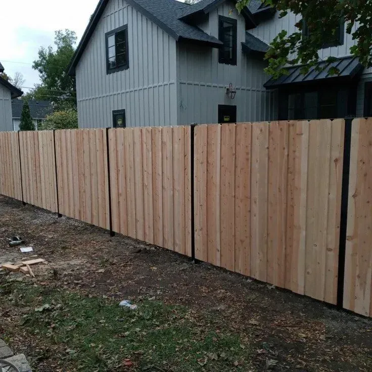 Wooden fence with black posts in front of a gray house.