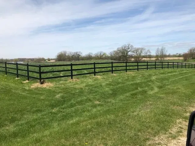 Black wooden fence in a grassy field under a partly cloudy sky.