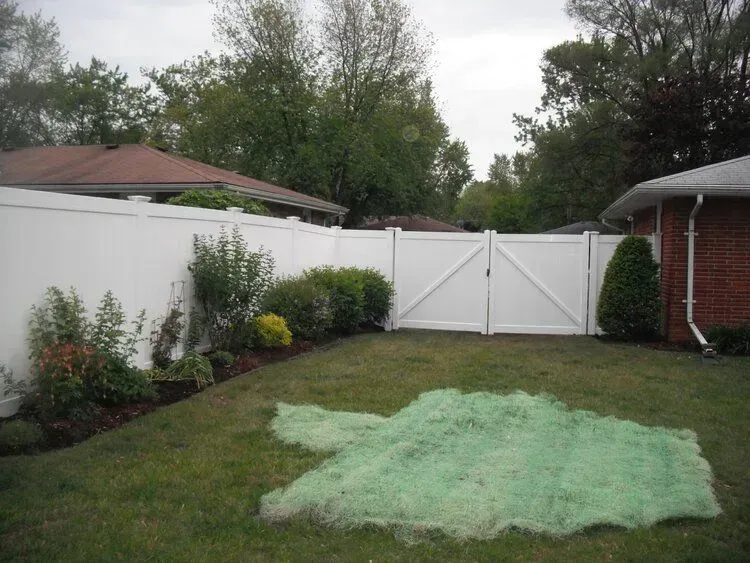 White fence and gate enclosing a grassy backyard with a pile of green netting.