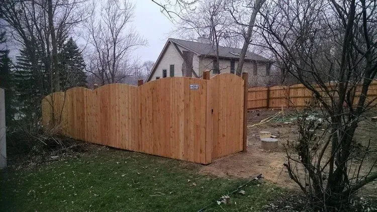 Wooden fence surrounding a backyard with a house in the background. Overcast day.