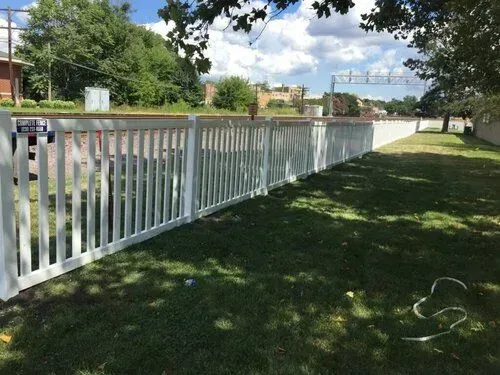 White picket fence along a grassy area, trees in background, sunny day.