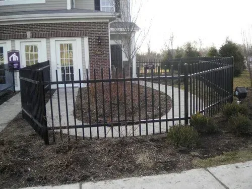 Black metal fence enclosing a circular garden bed in front of a building with white doors.