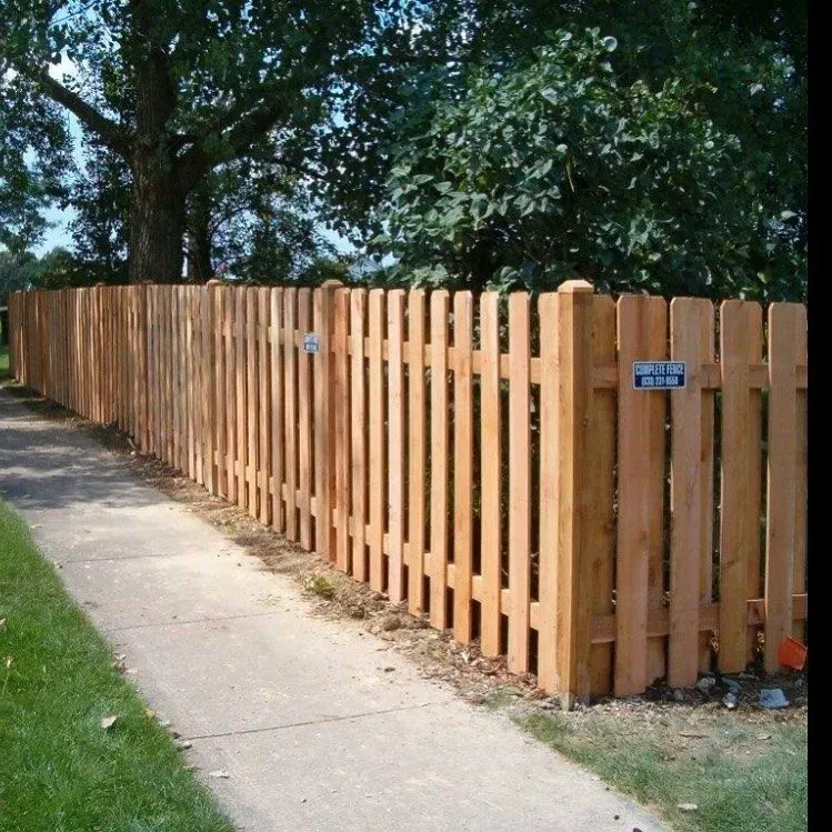 Wooden picket fence along a sidewalk, with trees in the background.