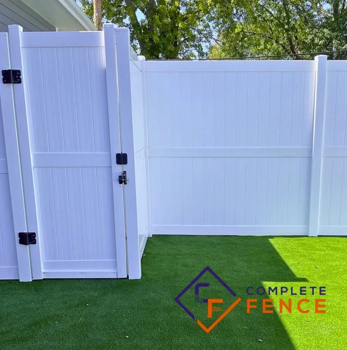 White vinyl fence with gate, black hardware, on green lawn; sunny outdoors.
