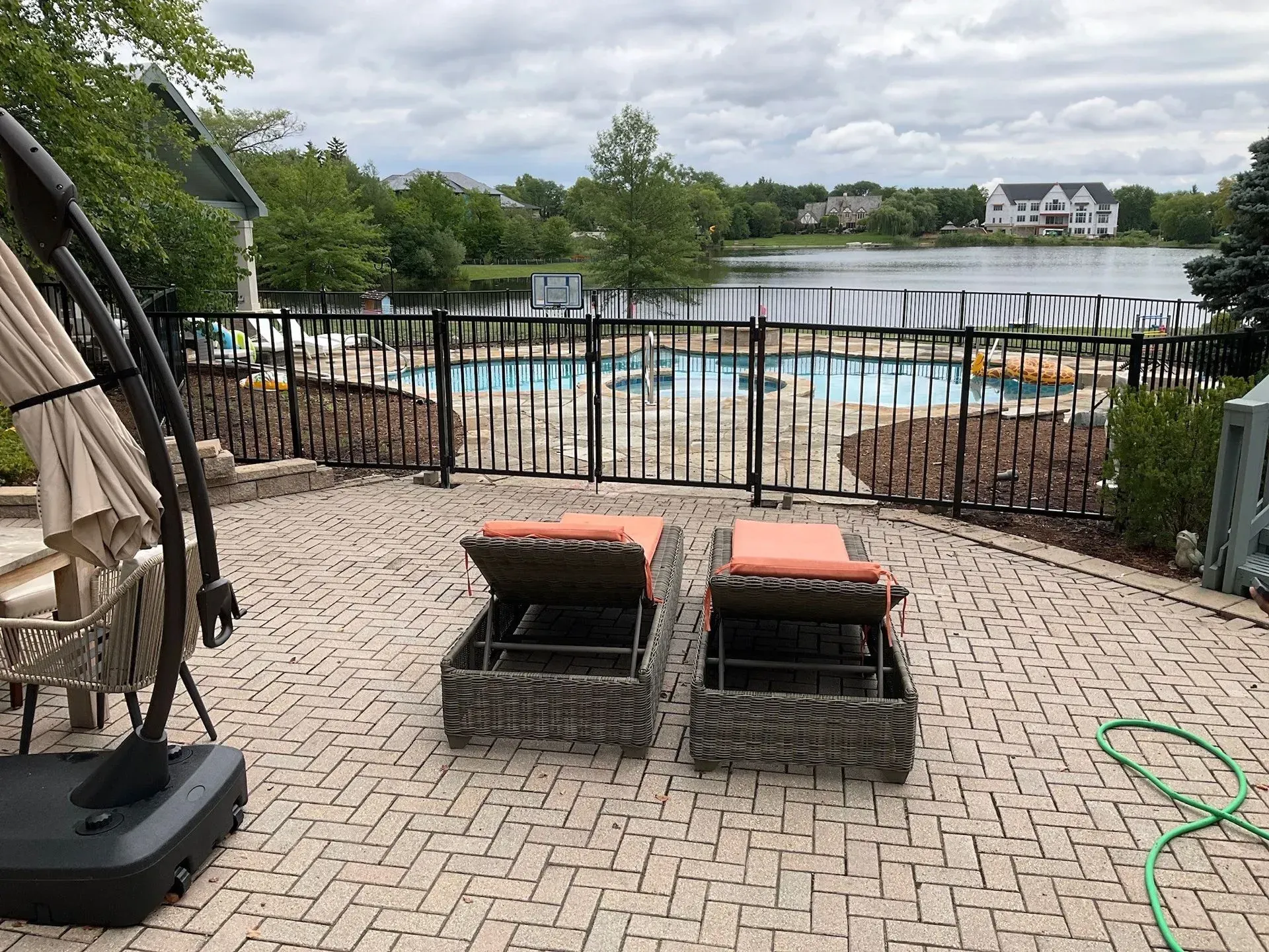 Patio with two lounge chairs, overlooking a fenced-in pool and lake. Overcast sky.