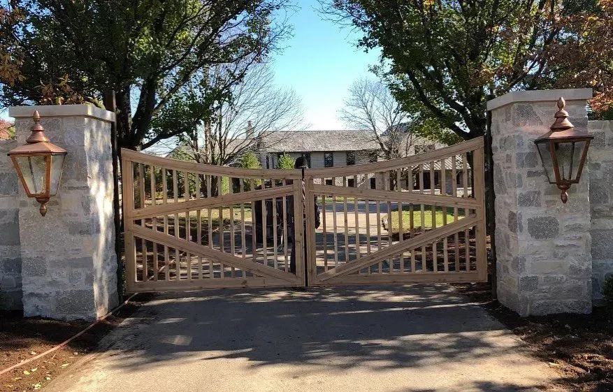 Wooden gate entrance to a house, flanked by stone pillars with copper lanterns.