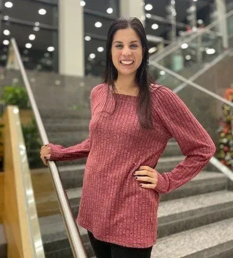 Woman in burgundy sweater, smiling, standing on stairs, hand on hip.