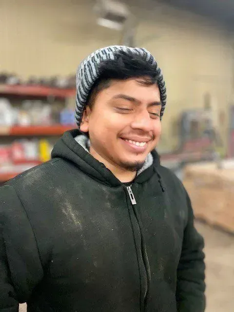 Man wearing a black coat and striped beanie, smiling with eyes closed indoors.