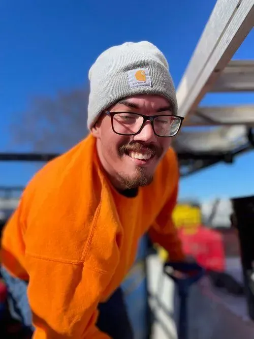 Man wearing orange sweatshirt and gray beanie smiles outdoors.