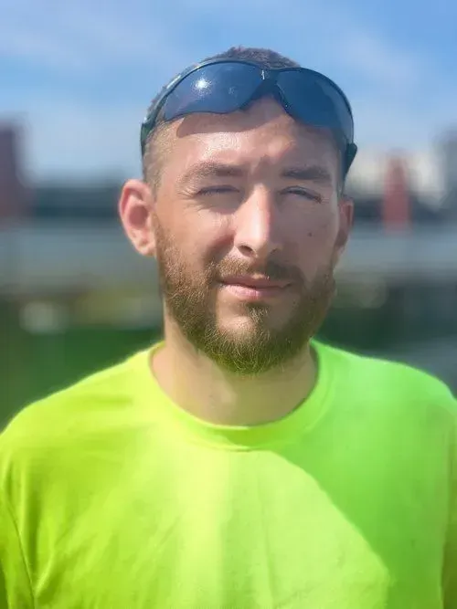 Man wearing sunglasses on head, green shirt, looking at the camera outdoors.