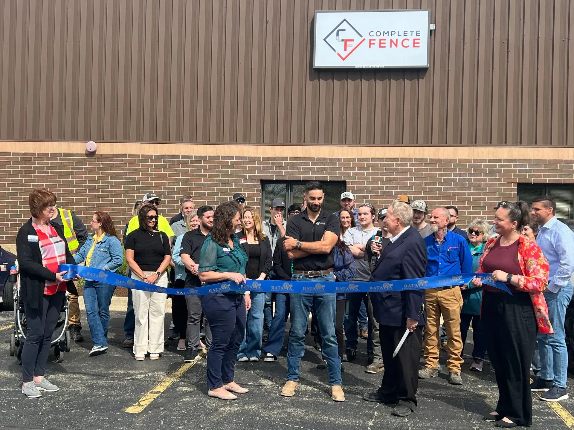 People cutting a blue ribbon in front of a building with a 