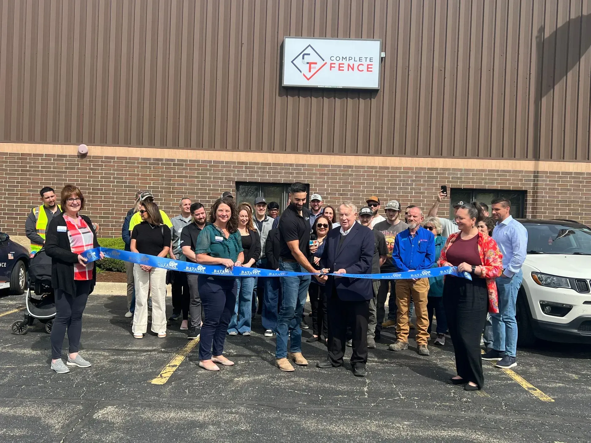 People cutting a blue ribbon in front of a building with a sign that says 