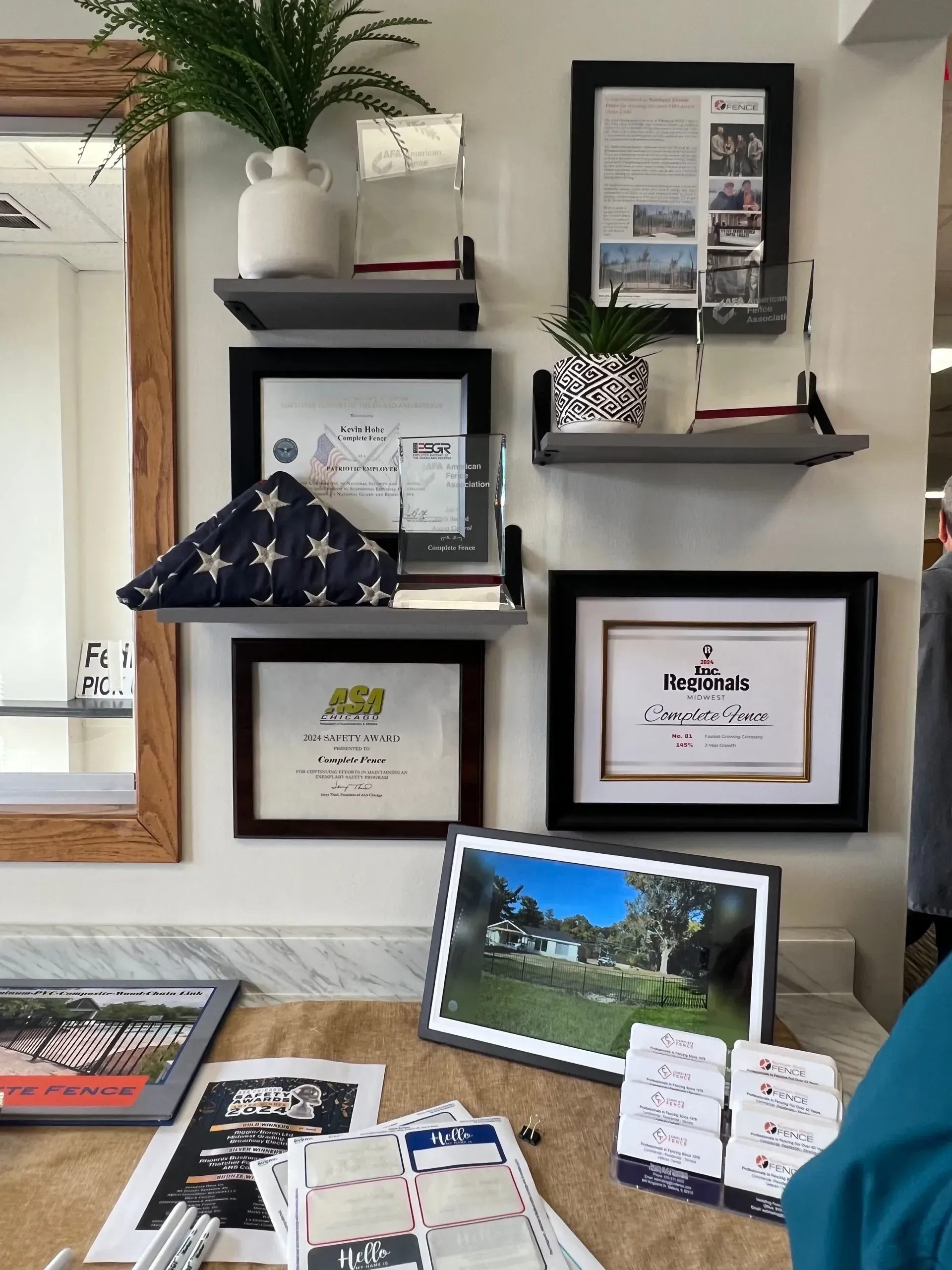 Display of framed documents, a folded flag, and photographs on shelves and a countertop.