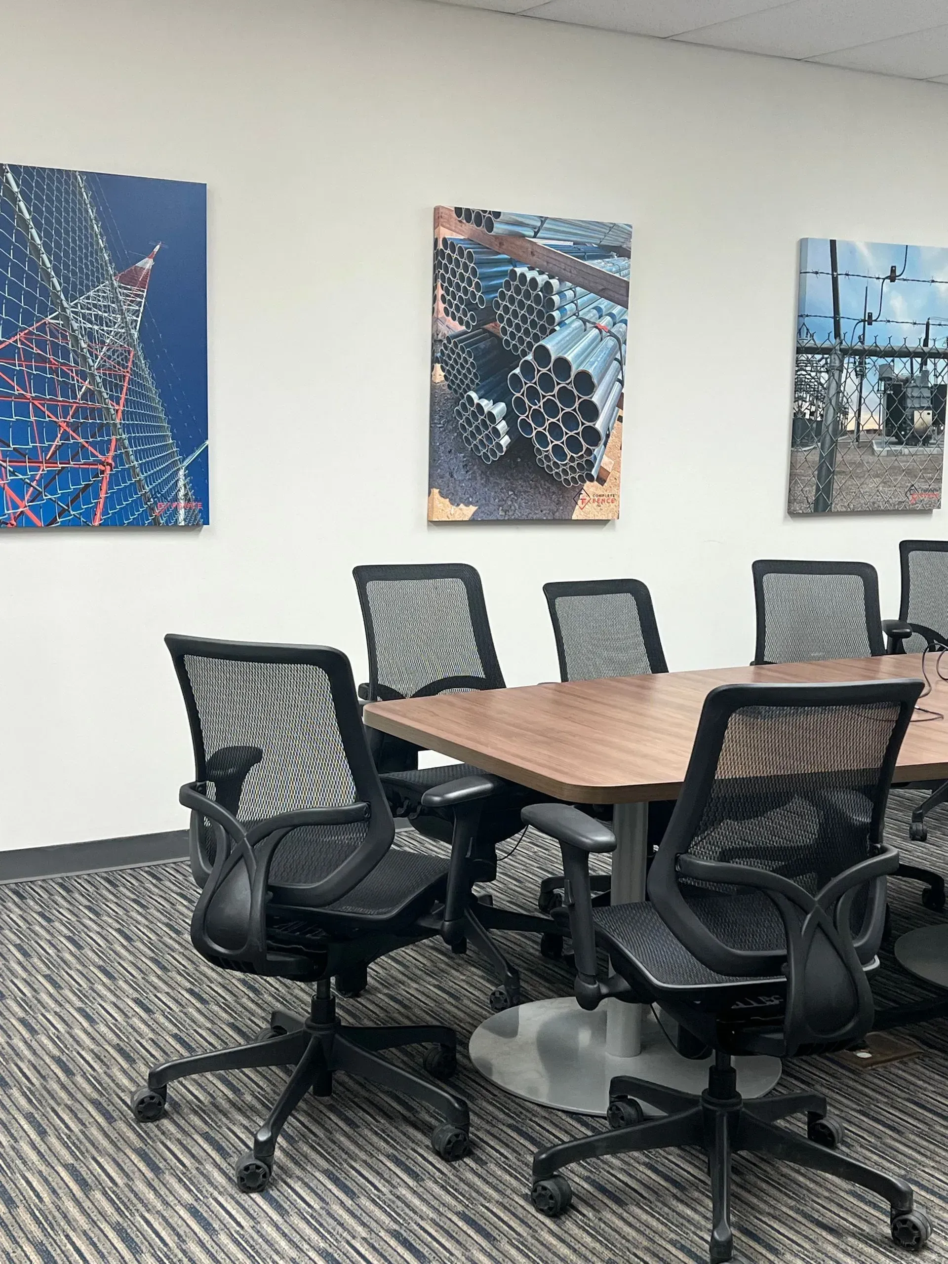 Conference room with table, black mesh chairs, and three abstract paintings on the wall.