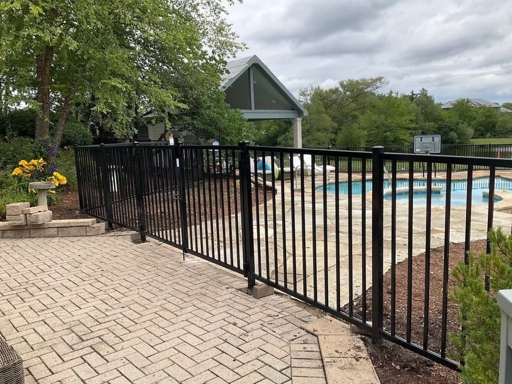 Black metal fence next to a brick patio, with a pool in the background under a cloudy sky.