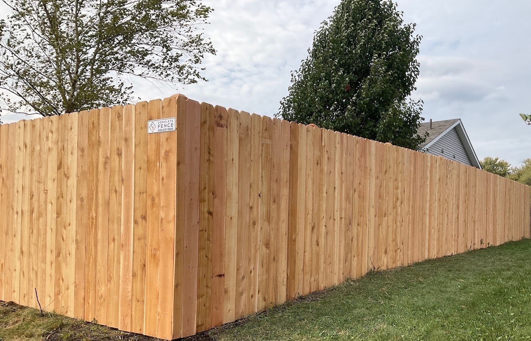 Wooden privacy fence bordering a grassy yard under a cloudy sky.