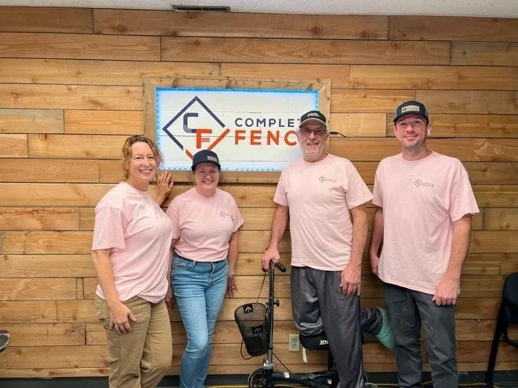 Four people wearing pink shirts pose in front of a wood-paneled wall with a sign that reads 