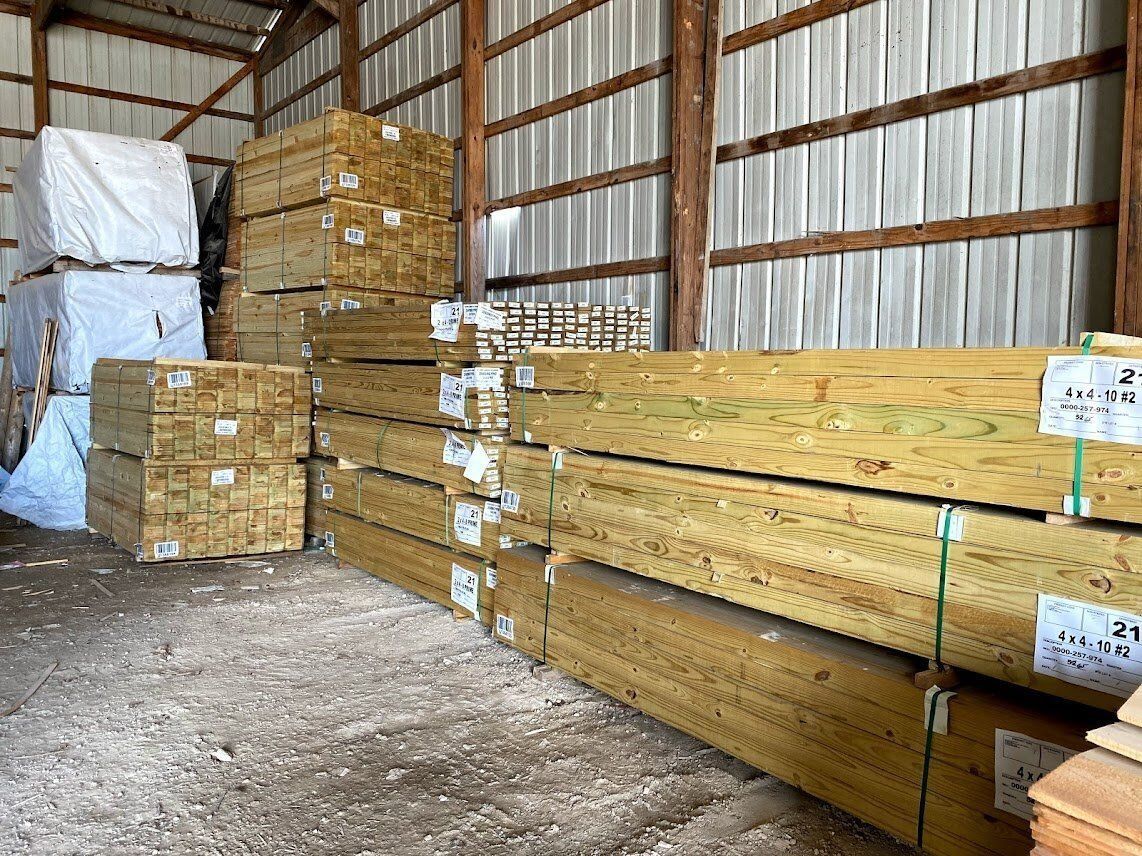 Stacks of lumber inside a wooden-framed warehouse. Some bundles are wrapped in white.