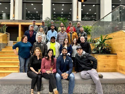 Group photo: diverse people posing on steps, in a modern building with wooden accents and large windows.