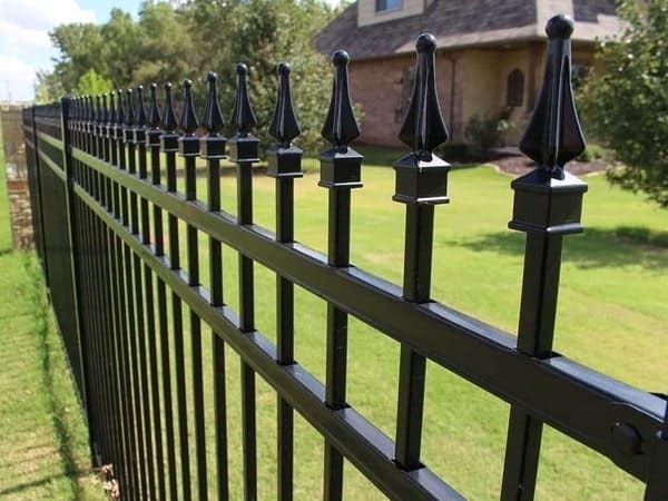 Black metal fence with decorative finials in front of a house and green lawn.