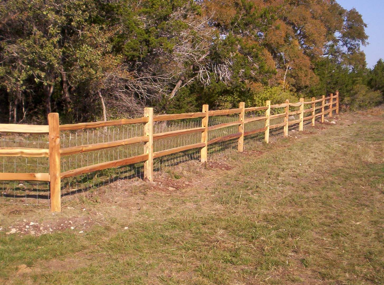 Wooden split-rail fence in a grassy field, with trees in the background.
