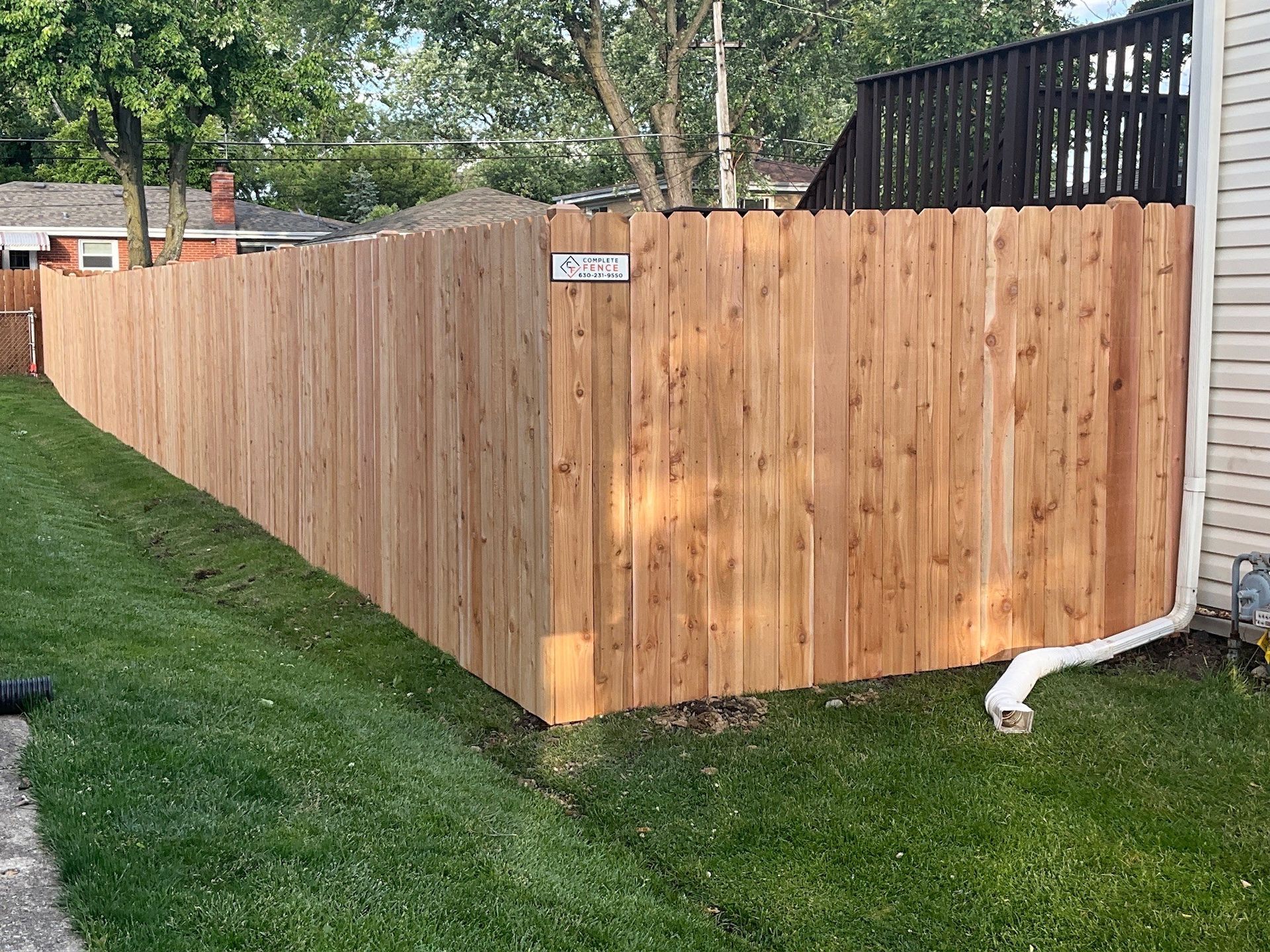 Wooden fence in backyard, on a grassy hill, next to a house with white siding.