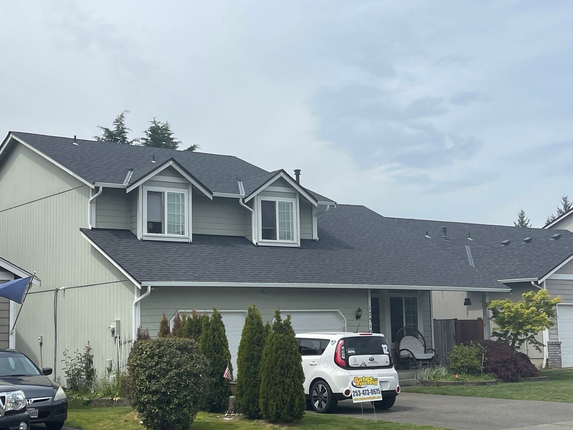 Light green house with a dark gray roof; white car in driveway. Overcast sky.