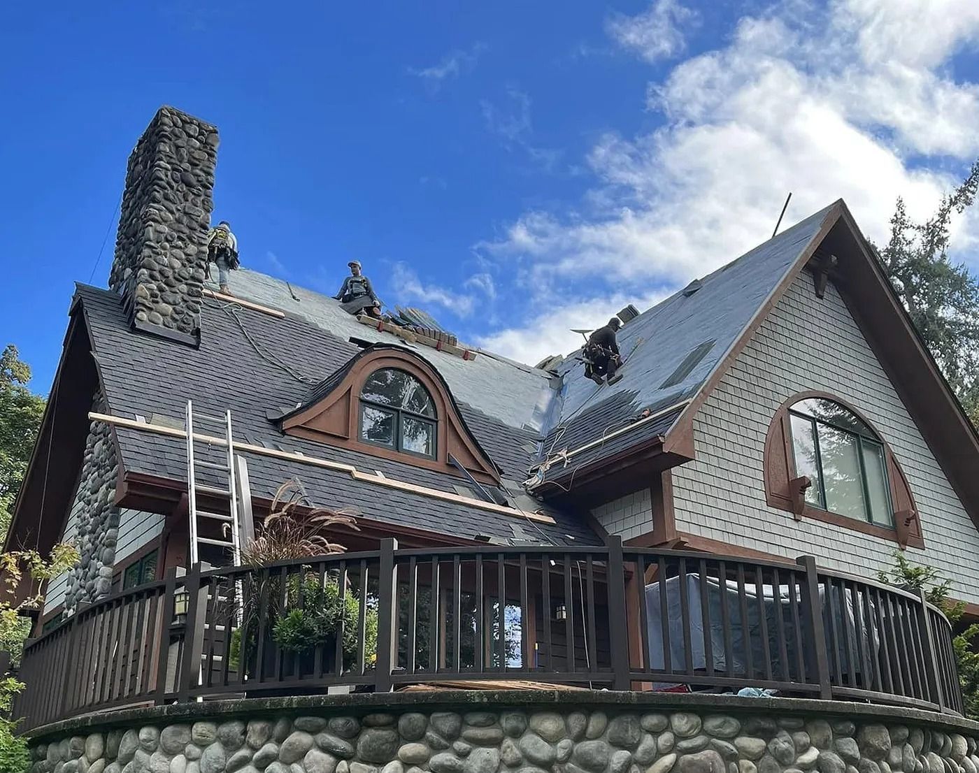 House with dark roof tiles, chimney, and stone facade; blue sky.