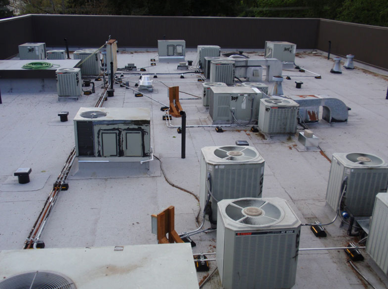 A flat commercial roof with multiple HVAC units, pipes, and other equipment.