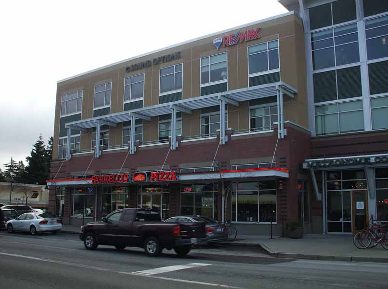 Building with bank and pizza restaurant, red brick facade, awnings, cars parked in front.