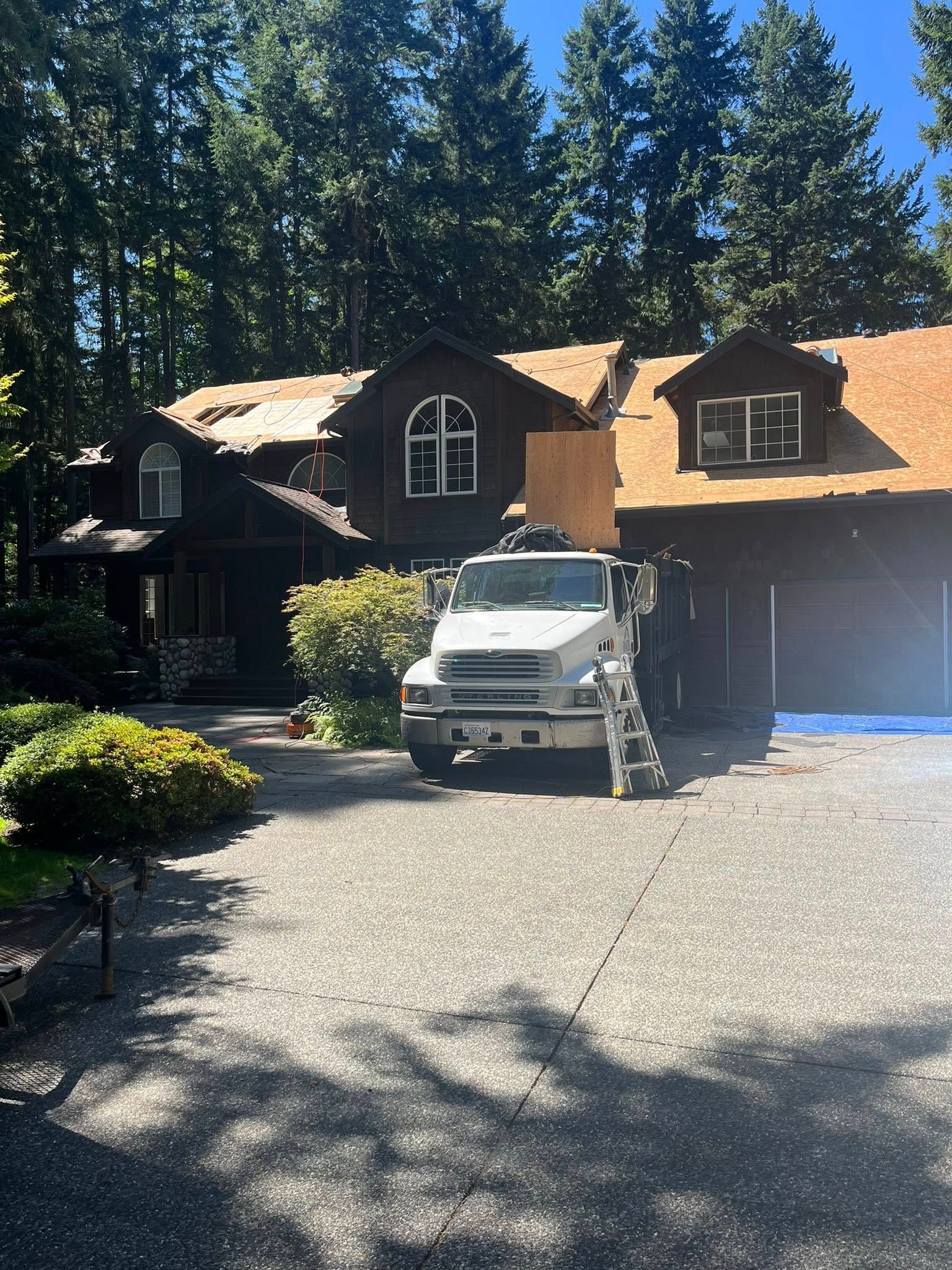 A truck parked in front of a house with partially removed roofing on a sunny day.