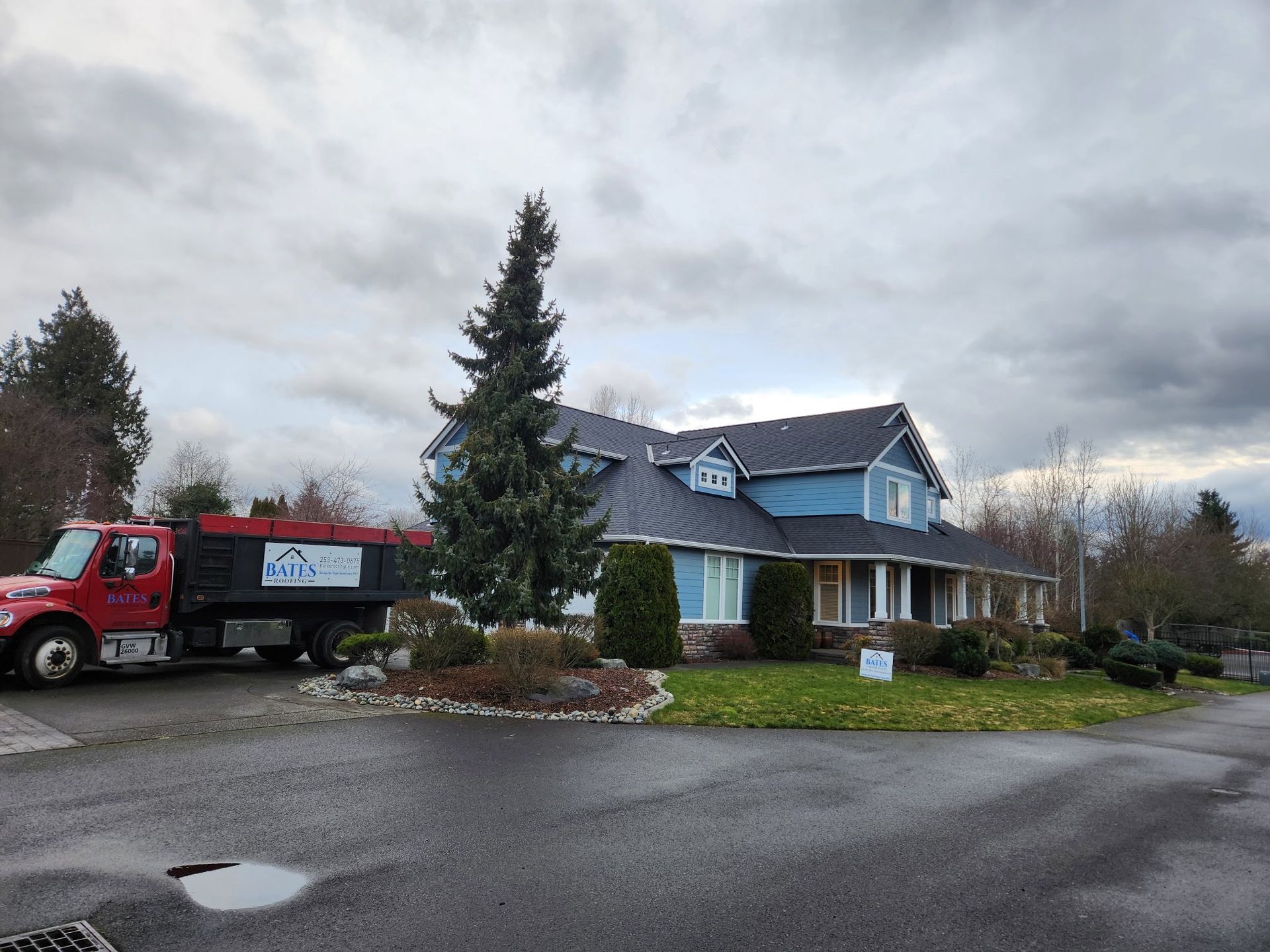 Blue house with dark roof; red dump truck parked in front. Cloudy sky.
