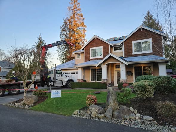 Crane removing roofing material from a two-story house with brown siding. Truck parked in the driveway.